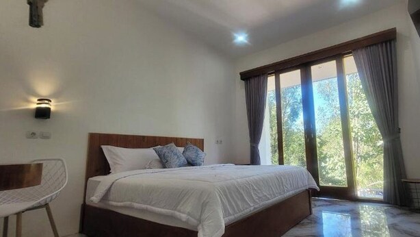 A bedroom with a large bed, a chair, a window with curtains, and a wall-mounted shelf. - Umah Yugadi Bali (Bali)