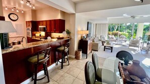 A modern kitchen with a central island, bar stools, and a dining area with a glass table and chairs.