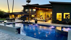 Ein modernes Haus mit Swimmingpool, Gartenmöbeln und einer gut beleuchteten Terrasse.