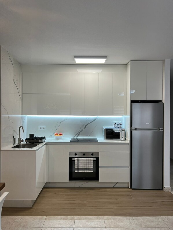 A modern kitchen with white cabinetry, a stainless steel refrigerator, a built-in oven, and a microwave.