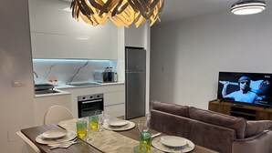 Un soggiorno moderno con angolo pranzo, cucina e televisione che mostra un evento sportivo.