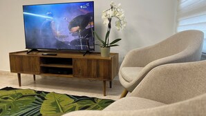 Un televisore su un supporto in legno, un'orchidea in vaso e una poltrona beige in un soggiorno.
