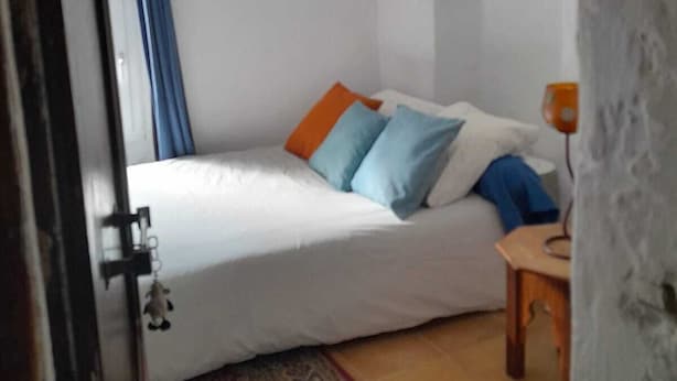 Ein Schlafzimmer mit Bett, Kissen, einer Hängelampe, einem kleinen Tisch und einem Teppich.