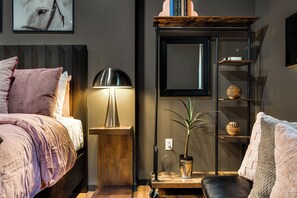 Een netjes opgemaakt slaapkamer met een bed, bedlampje, nachtkastje en een bloempot.