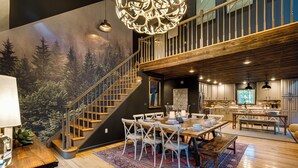Een ruime woonkamer met een houten trap, een eettafel met stoelen, en een keuken met moderne apparatuur.