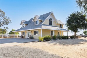 Une maison à deux étages avec un toit à pignon, une véranda et une allée bordée d’une clôture.