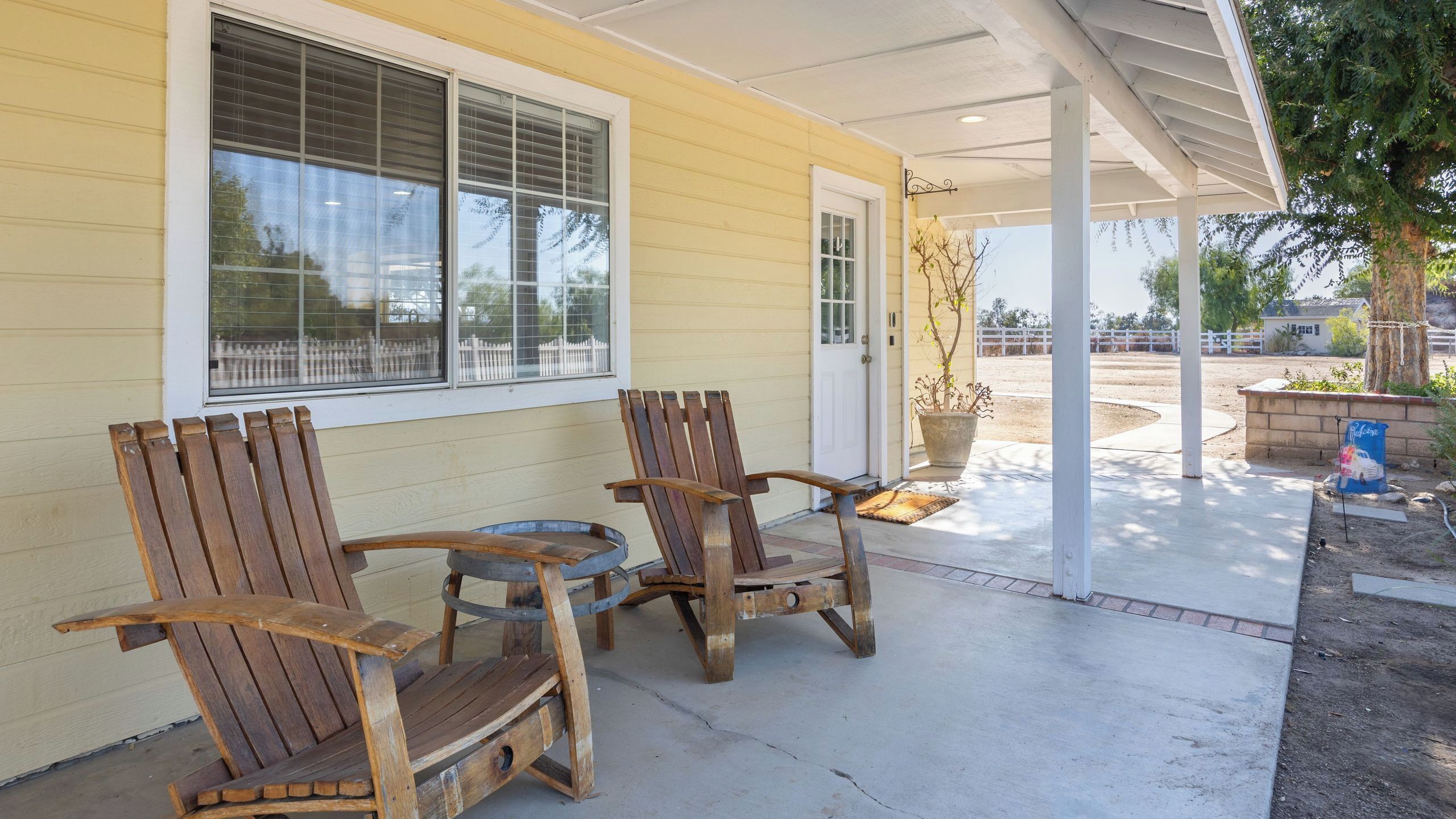 A covered porch with two wooden Adirondack chairs and a potted plant.