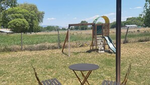An outdoor seating area with a table and chairs, a playground with a slide, and a covered structure.