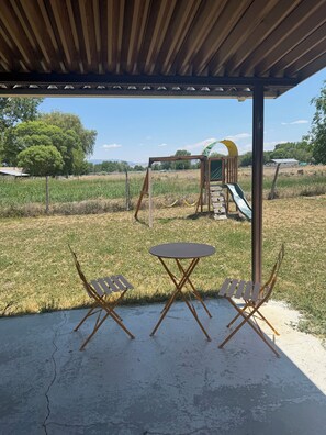 Ein Sitzbereich im Freien mit Tisch und Stühlen, ein Spielplatz mit Rutsche und eine überdachte Konstruktion.