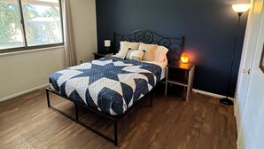 A bedroom with a bed, a nightstand, a lamp, and a window.