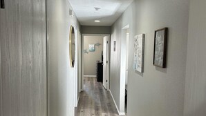 A hallway with wooden flooring, white walls, and a ceiling light.
