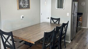 A dining room with a wooden table and chairs, a chandelier, a framed sign, and a refrigerator.
