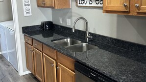 A modern kitchen with wooden cabinets, a stainless steel dishwasher, and a granite countertop.