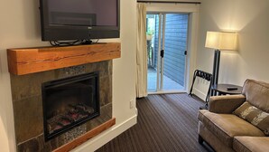 A living room with a fireplace, a flat-screen TV mounted above it, a sofa, and a lamp.
