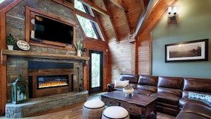 Una sala de estar acogedora con chimenea de piedra, sofá de cuero y televisor de pantalla plana sobre la chimenea.