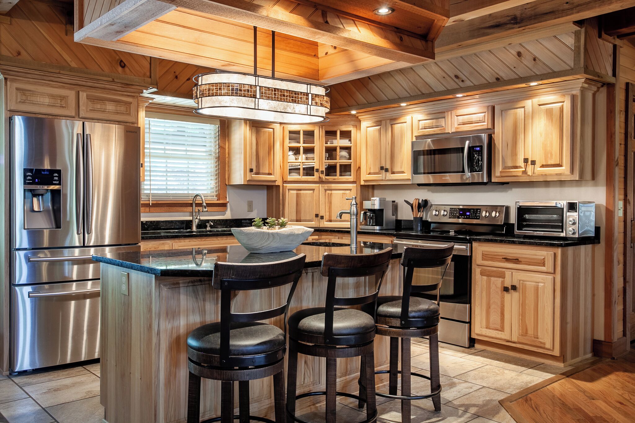 A modern kitchen with wooden cabinets, stainless steel appliances, and a central island with bar stools.