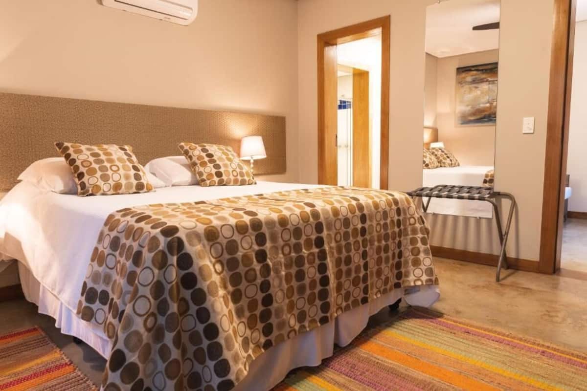 Hotellihuone, jossa on sänky, yöpöytä, tuoli ja ovi, joka johtaa toiseen huoneeseen.