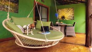 Una poltrona a dondolo in vimini con un cuscino verde e un cane seduto sopra, un laptop e un vaso con fiori su un tavolo.