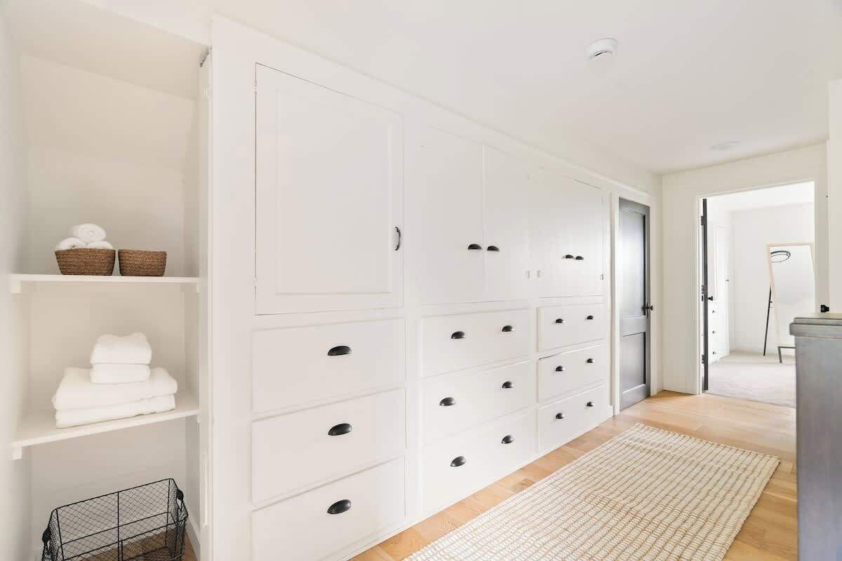Ein geräumiges Zimmer mit einem großen, weißen Kleiderschrank, Holzboden und einem weißen Teppich.