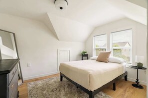 A bedroom with a bed, a dresser, a small table, and a window. - Contemporary Camas Retreat (Camas)