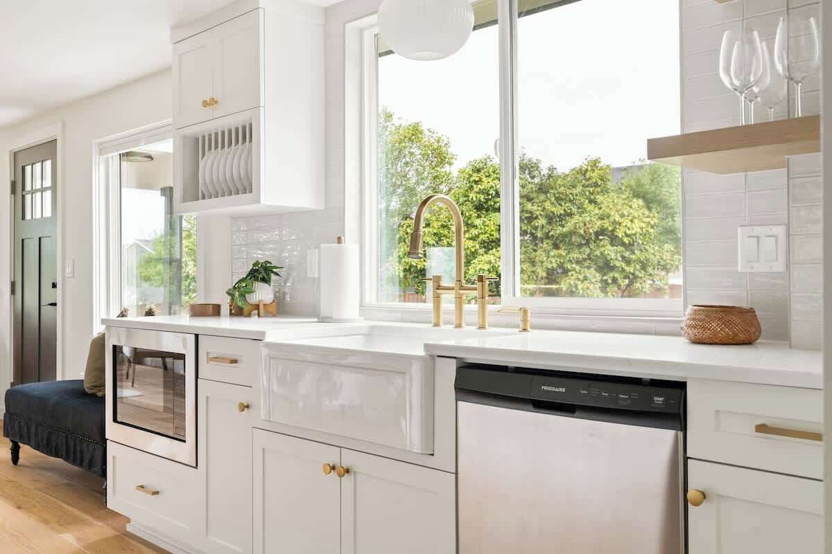 Une cuisine moderne avec des meubles blancs, un lave-vaisselle intégré et une fenêtre donnant sur un espace verdoyant.