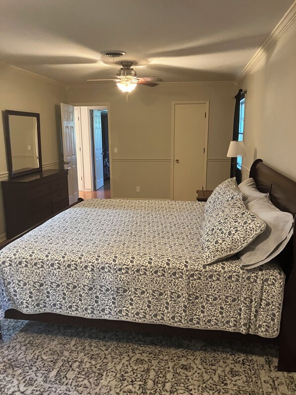 A bedroom with a bed, a dresser, a mirror, a ceiling fan, and a door leading to another room.