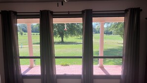 Een kamer met grote ramen, een kamerbreed tapijt met dessin en uitzicht op een park met bomen en gazon.