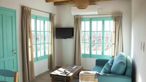 A cozy room with a wooden ceiling, a flat-screen TV mounted on the wall, a blue sofa, a wooden coffee table, and a window with curtains. - Finca Rosablanca (Tunuyan)