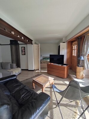 A living room with a black leather sofa, a wooden coffee table, a TV on a wooden cabinet, and a wicker chair.