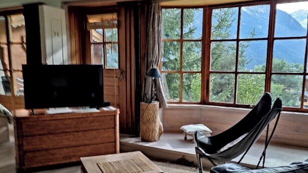 Un salón acogedor con un sofá de madera, un televisor y un amplio ventanal con vistas a la montaña.