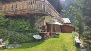 Una casa rústica de madera con un balcón, un jardín pequeño y una terraza de madera.