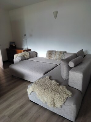 A modern living room with a grey sectional sofa, a fluffy throw blanket, and a wooden side table with a lamp.