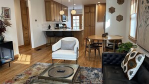 A modern living room with a sofa, a coffee table, and a rug. There is a kitchen area with wooden cabinets and a dining table.