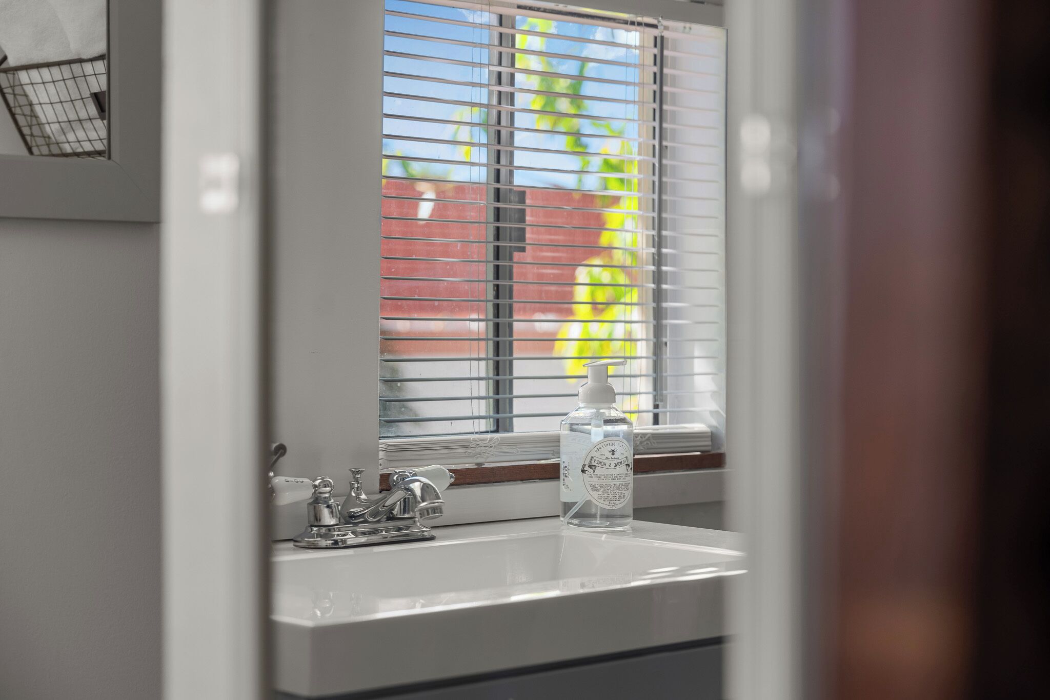 Une salle de bain avec une fenêtre, un lavabo et un flacon de gel hydroalcoolique.
