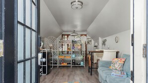 Ein gemütliches Zimmer mit einem türkisfarbenen Sofa, einem gemusterten Teppich, einem Metallregal mit verschiedenen Gegenständen und einem kleinen Tisch mit einer Lampe.