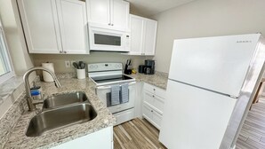 A compact kitchen with white cabinets, a built-in microwave, a stove, a sink, and a refrigerator.