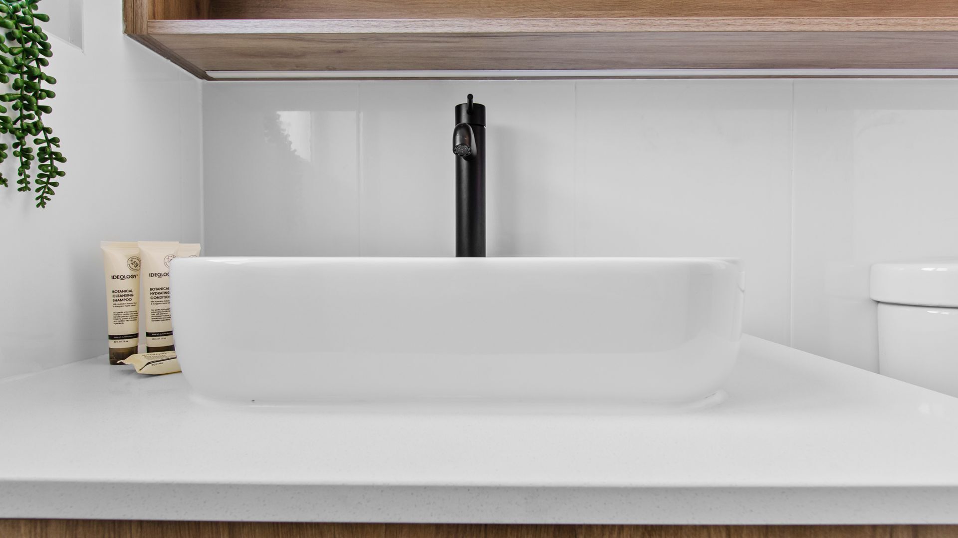 Een wit badkamermeubel met een zwart kranenwerk, een witte werkblad en een houten kast erboven.