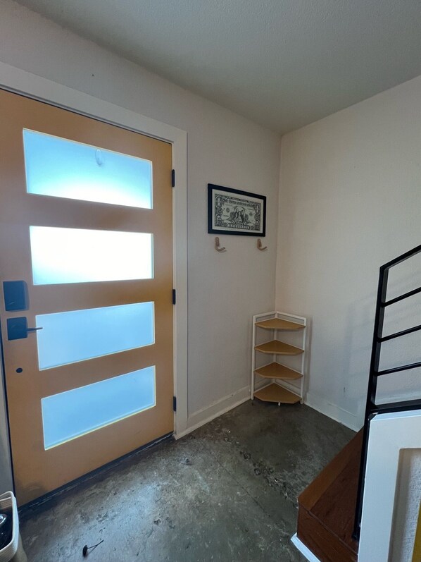A room with a wooden door, a framed picture on the wall, and a small white shelf.