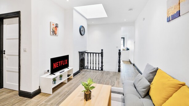 A modern living room with a flat-screen TV, a coffee table with a plant, and a grey sofa with yellow cushions. - MODERN DUPLEX APARTMENT LOCATED NEAR CITY CENTRE - FREE PARKING, WI FI & NETFLIX (Reading)