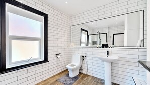 A modern bathroom with white tiled walls, a wooden floor, a toilet, a sink, and a large mirror. - MODERN DUPLEX APARTMENT LOCATED NEAR CITY CENTRE - FREE PARKING, WI FI & NETFLIX (Reading)