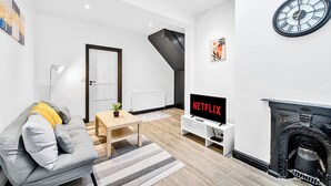 A modern living room with a sofa, a coffee table, a TV, a fireplace, and a staircase. - MODERN DUPLEX APARTMENT LOCATED NEAR CITY CENTRE - FREE PARKING, WI FI & NETFLIX (Reading)