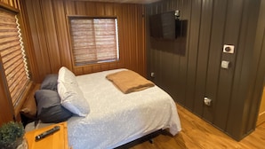A bedroom with a bed, wooden walls, a ceiling fan, a TV, and a window with blinds. - Copper Lodge - Lake Miltona
License #:  1999 (Miltona)