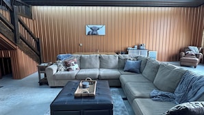 A spacious living area with a large sectional sofa, a coffee table, and a wooden wall with a framed picture. - Copper Lodge - Lake Miltona
License #:  1999 (Miltona)