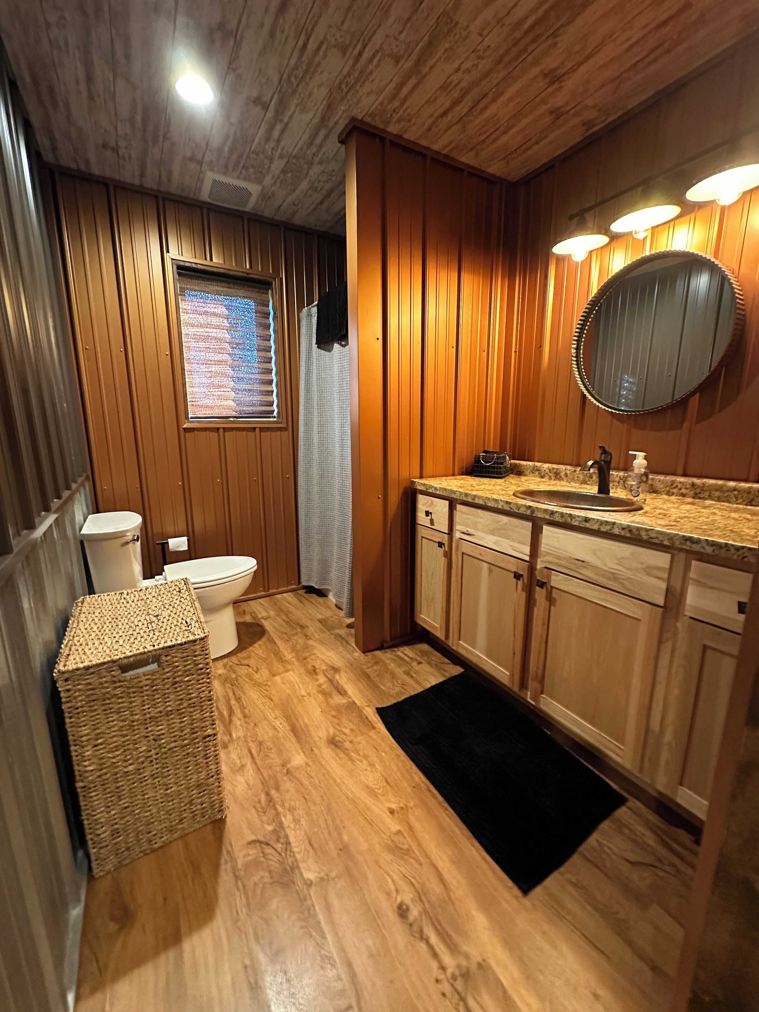 Une salle de bain aux murs lambrissés, équipée de toilettes, d’un lavabo et d’un miroir.