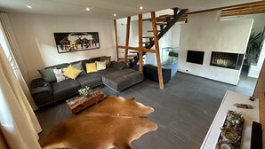 Una sala de estar moderna con un sofá gris, una escalera de madera y un tapete grande de cuero de vaca.
