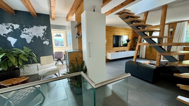 Un espacio habitable moderno con una escalera de cristal, un mural de un mapa mundial y un techo de madera.