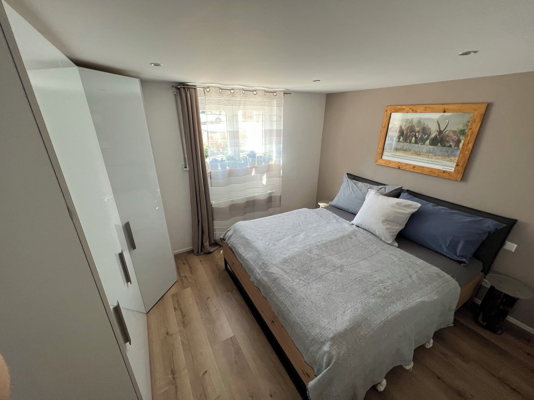 A bedroom with a bed, a wardrobe, a window with curtains, and a painting on the wall.
