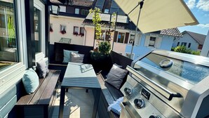 Un patio al aire libre con una parrilla, asientos y vistas de edificios cercanos.
