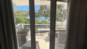 A room with a sliding glass door leading to an outdoor area with a pool, lounge chairs, and palm trees.