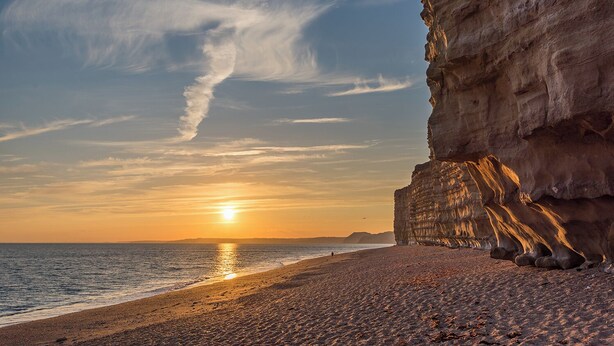 A coastal sunset with a rocky cliff and a beach.